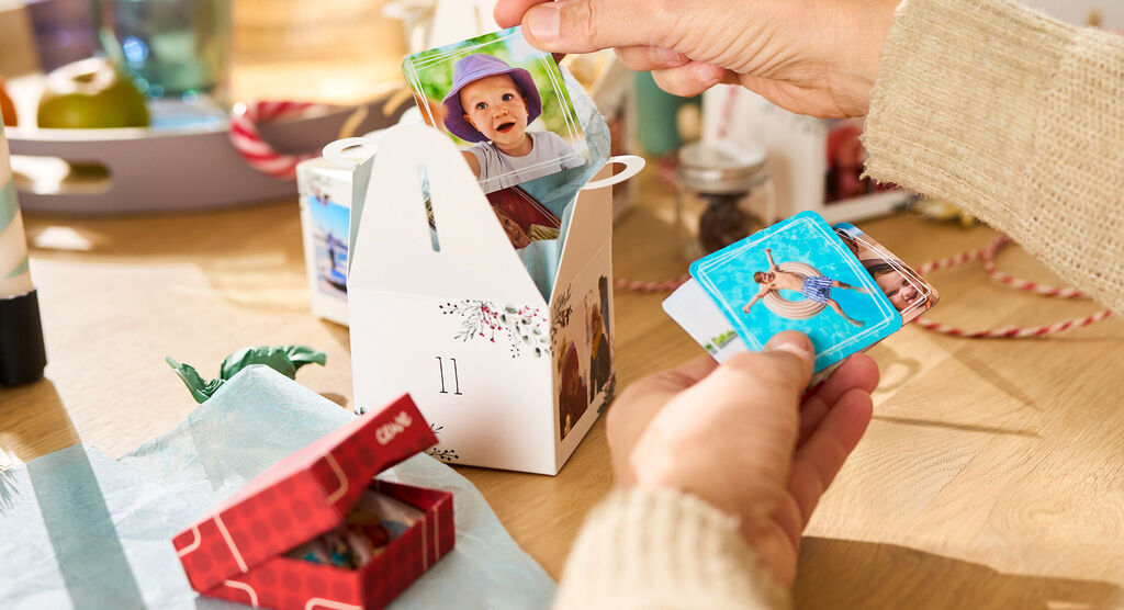 "Eine Person steckt kleine Fotokärtchen mit bunten Motiven in eine weiße Geschenkbox von CEWE