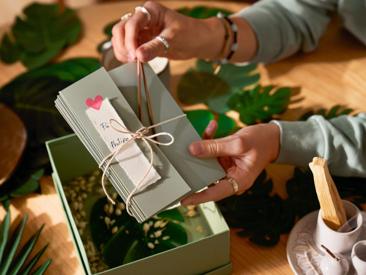 Eine Frau verziert ein Geschenk mit Räucherstäbchen und legt es in eine Geschenkbox.