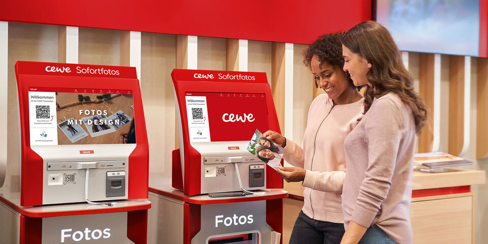Zwei Personen bedienen einen CEWE Selbstbedienungsfototerminal zur Fotoauswahl