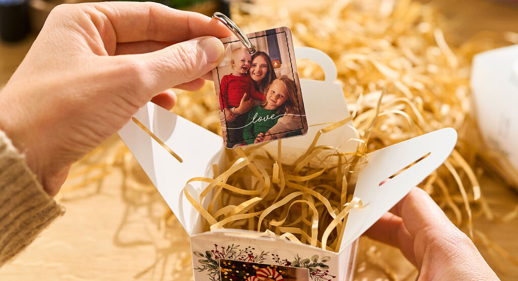 Eine Person befüllt eine mit Fotos bedruckte Schachtel mit Papierwolle und einem Foto-Schlüsselanhänger.