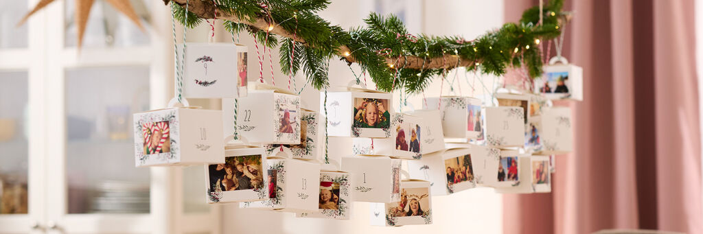 Ein weihnachtlich dekorierter Adventskalender aus 24 einzelnen Schachteln, die mit verschiedenen Fotos bedruckt sind.