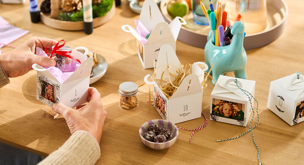 Mehrere kleine Geschenkboxen mit Fotos und bunten Bändern stehen liebevoll auf einem Tisch